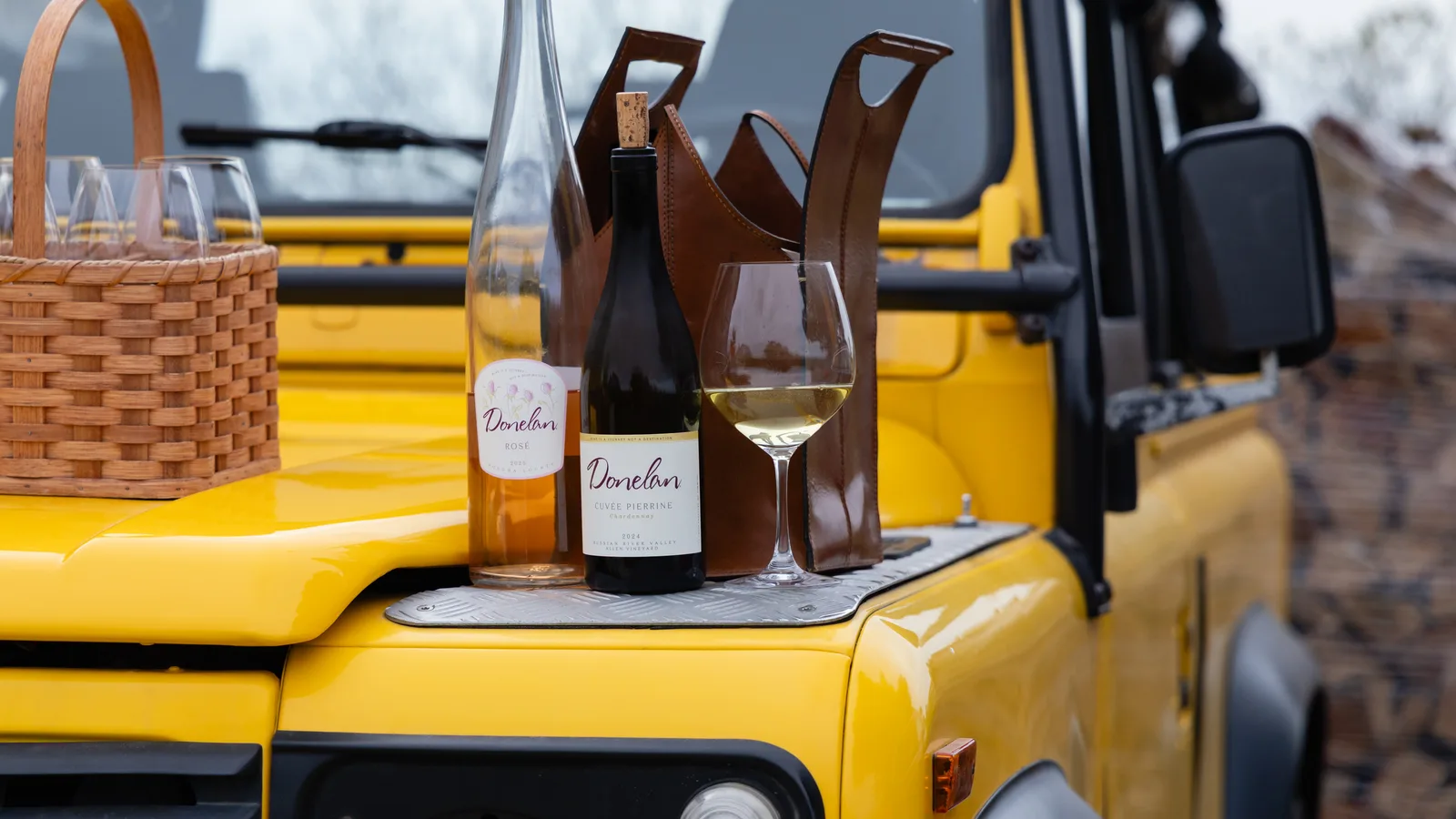 Donelan wine bottles and a poured glass on the hood of a yellow Land Rover Defender