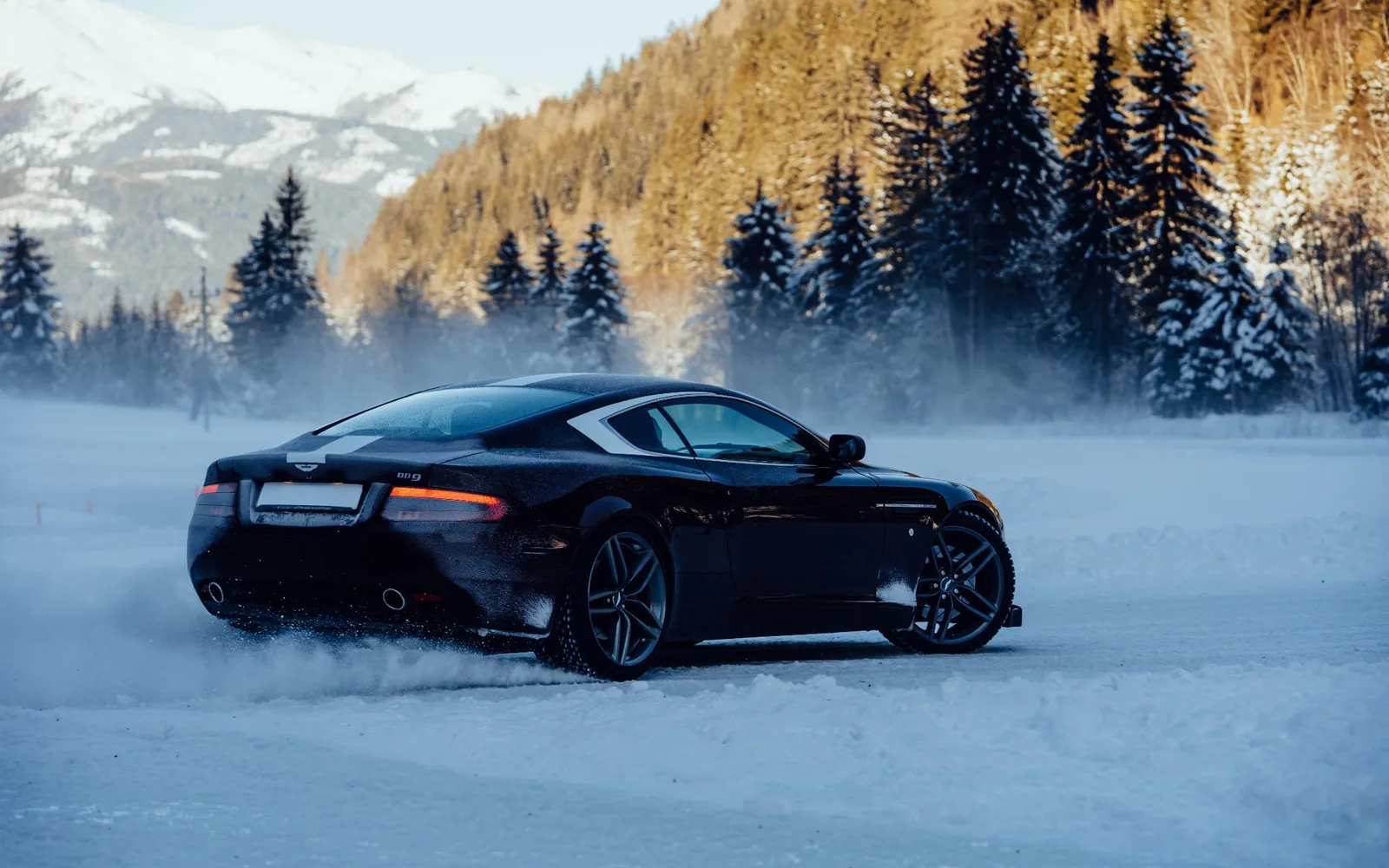 An Aston Martin sliding through snow on a frozen circuit among alpine trees