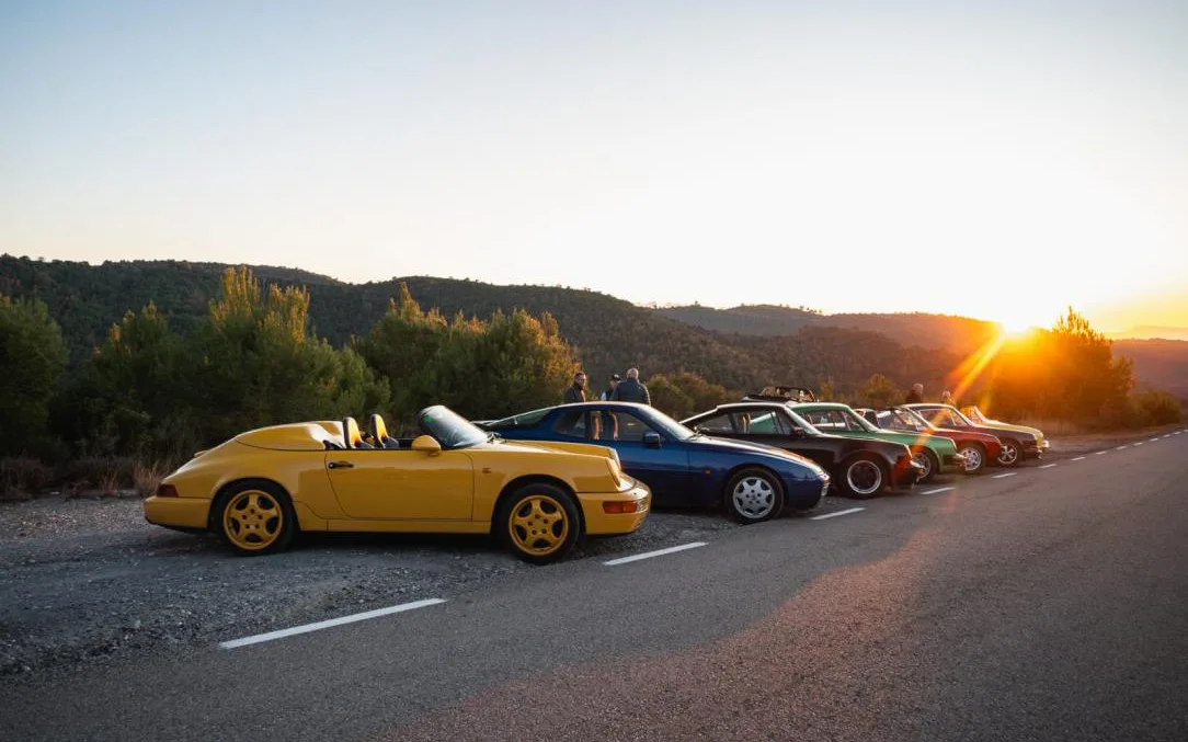 A line of classic Porsches parked on a mountain road at sunset