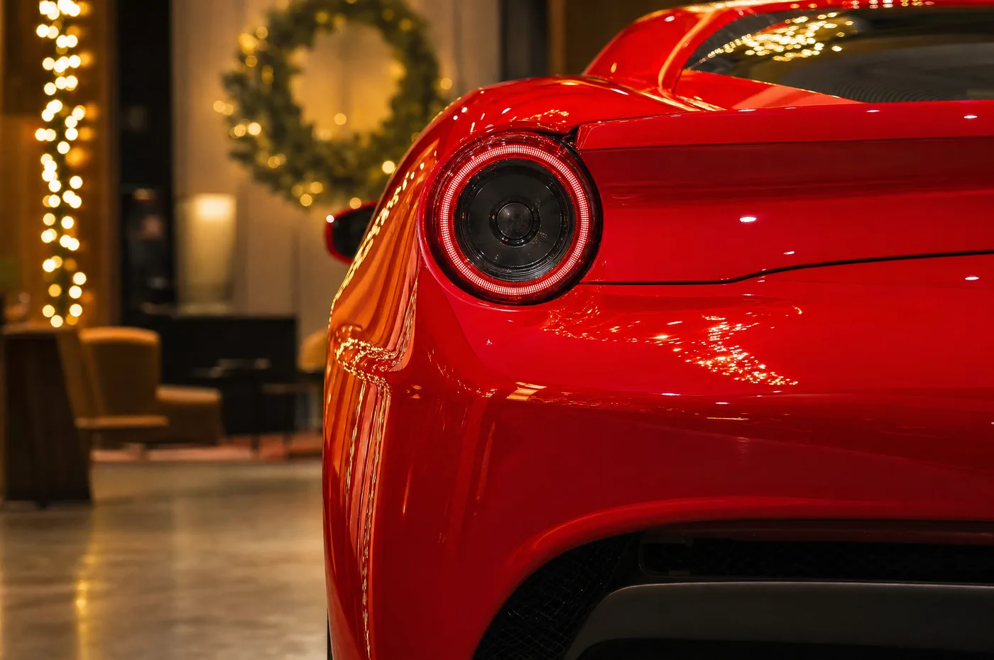 The round taillight of a red Ferrari with holiday lights and a wreath softly out of focus behind it