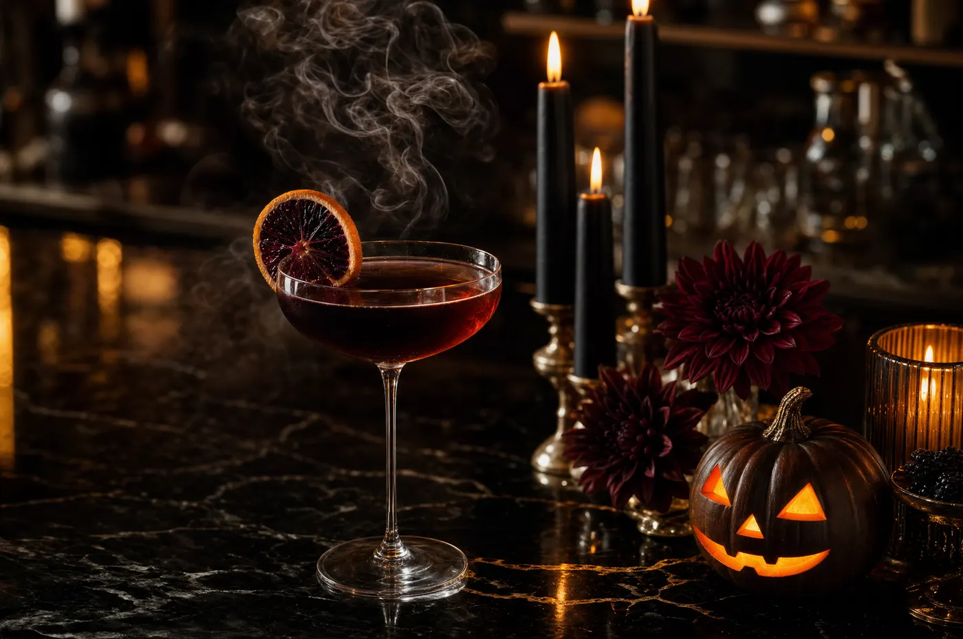 A dark red cocktail in a coupe with a smoking garnish beside black candles, dark dahlias and a small lit jack-o-lantern on a marble bar