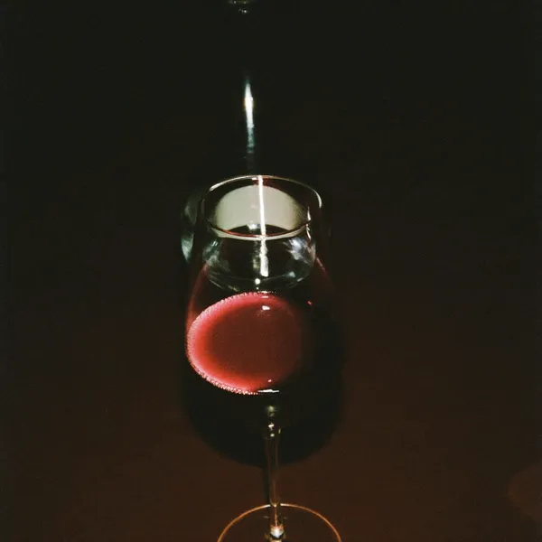 A glass of deep red wine backlit in low candlelight
