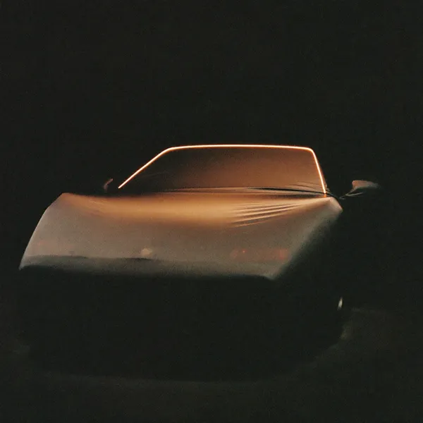 A covered car form under a sliver of rim light